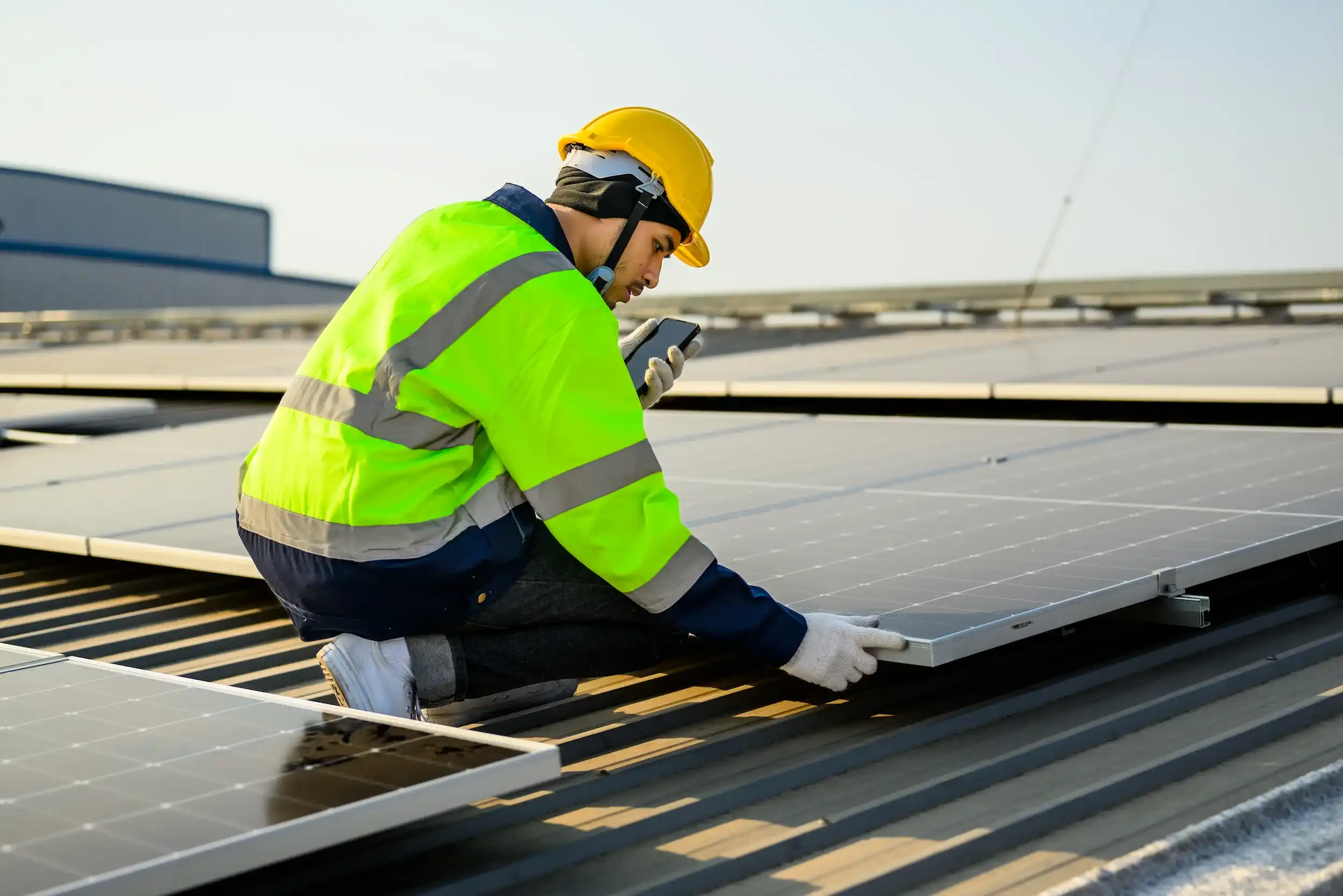 Technician adjusting a rooftop solar panel while checking measurements on a mobile device.