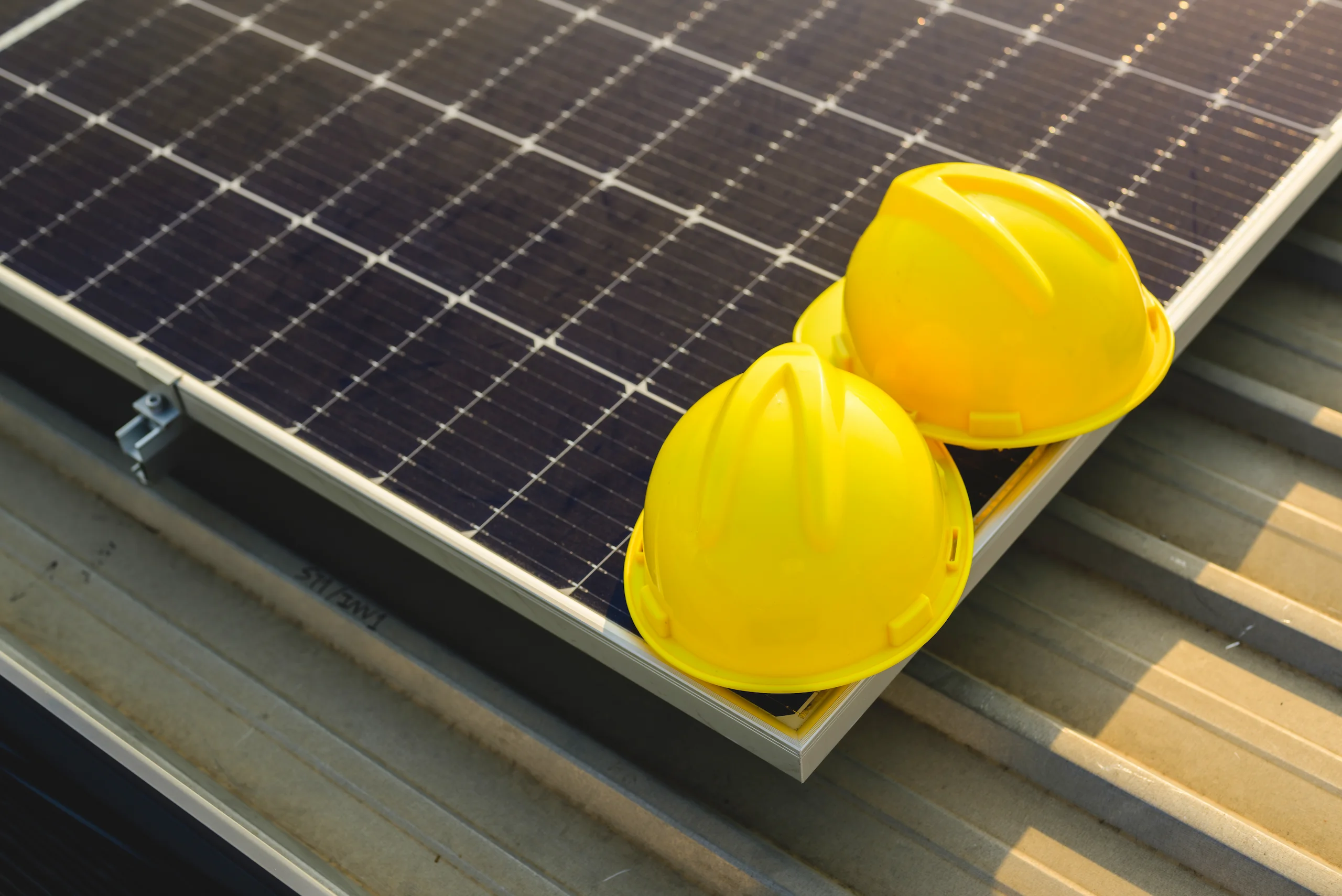 Two yellow safety helmets placed on the edge of a solar panel during a rooftop installation.