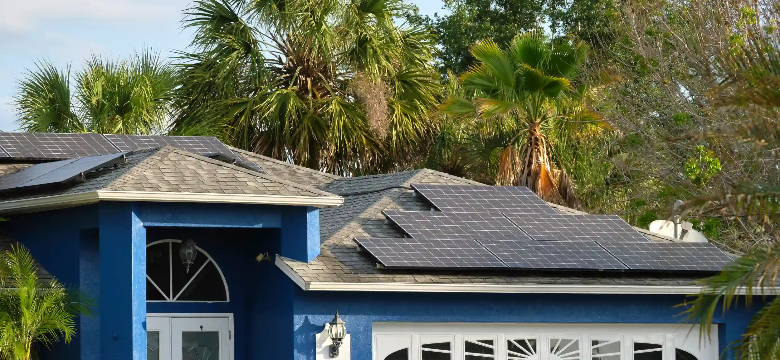 Residential solar panels installed on a tropical home surrounded by palm trees in Yeppoon.